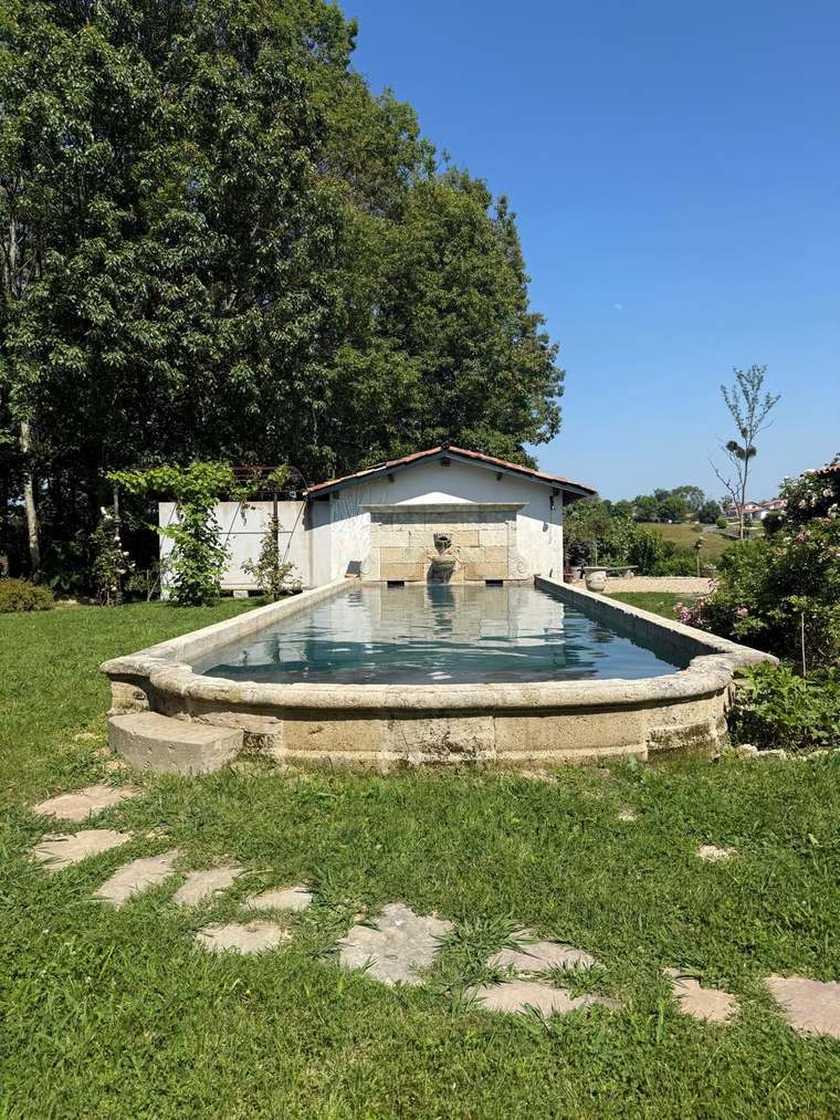 Bassin en pierre dans le jardin, devant une dépendance