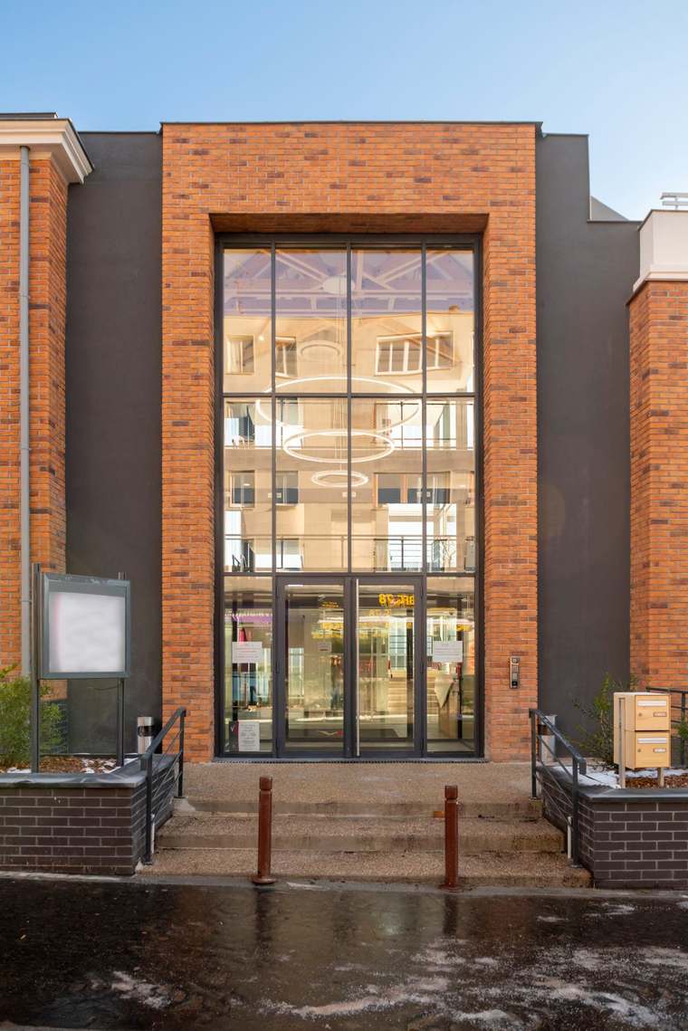 Entrée en brique et grande verrière ouvrant sur l'atrium