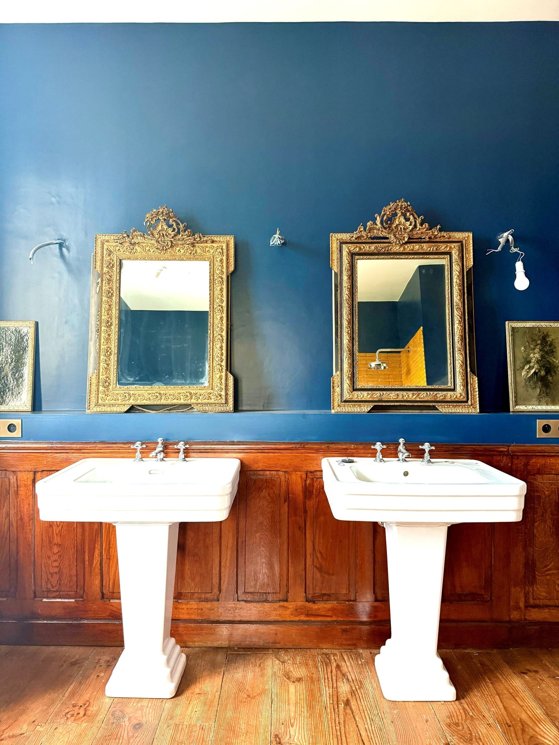 Deux vasques sous des miroirs dorés, mur bleu